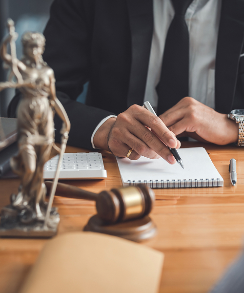 A focused lawyer taking notes on a notepad while seated at a desk in a professional office environment.